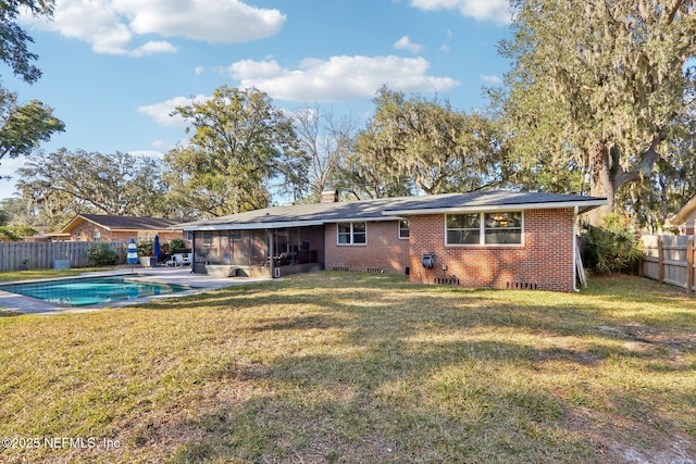 back of house featuring brick siding, a sunroom, a chimney, a yard, and a fenced backyard