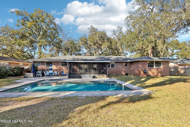 rear view of house with brick siding, a fenced in pool, a lawn, a chimney, and a sunroom