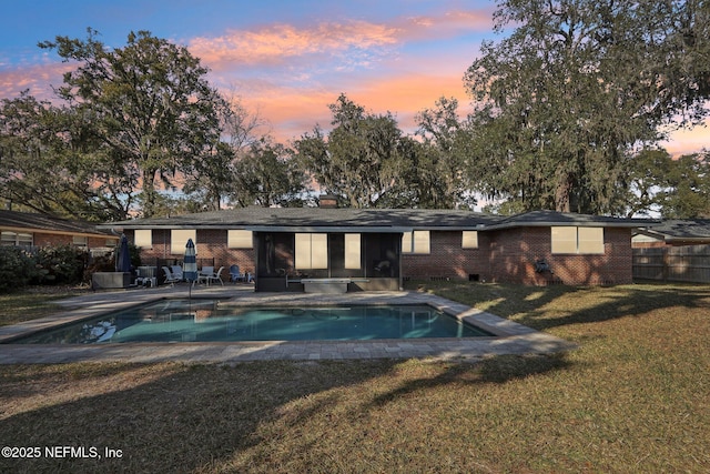 back of house at dusk featuring a patio, fence, an outdoor pool, a lawn, and brick siding