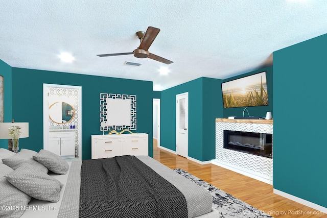 bedroom featuring wood finished floors, baseboards, visible vents, a fireplace, and a textured ceiling