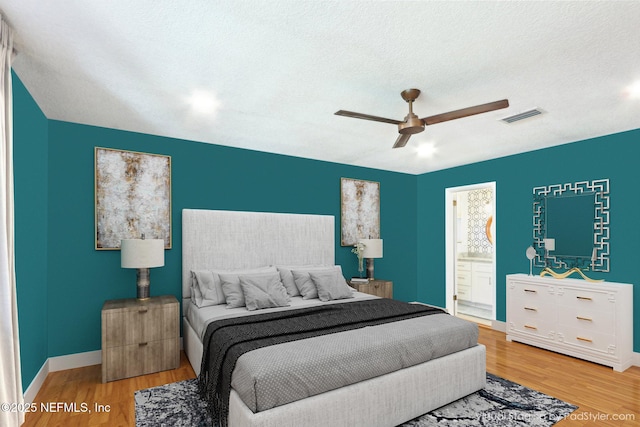 bedroom with visible vents, a textured ceiling, baseboards, and wood finished floors