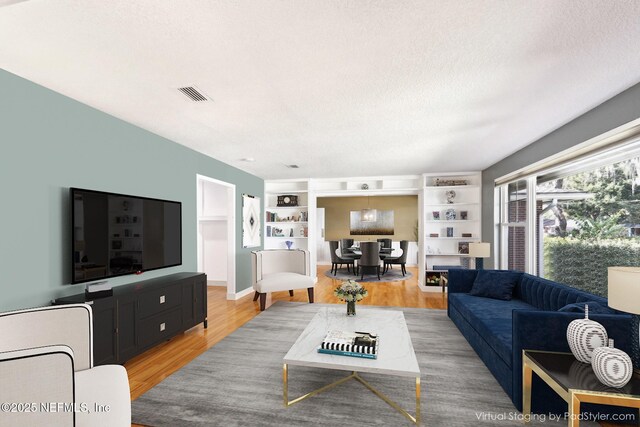 living area with built in features, visible vents, light wood finished floors, and a textured ceiling