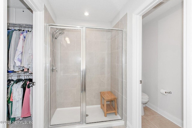 bathroom featuring tile patterned flooring, a textured ceiling, toilet, and walk in shower