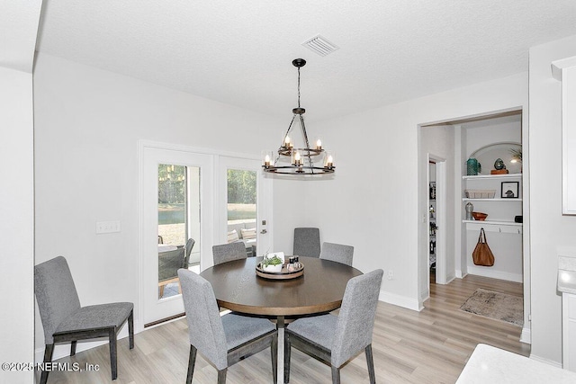 dining space with built in shelves, a chandelier, a textured ceiling, and light hardwood / wood-style flooring