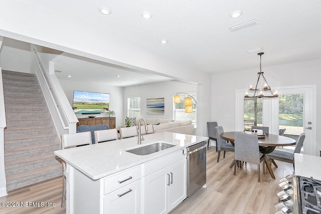 kitchen with decorative light fixtures, dishwasher, sink, white cabinets, and a center island with sink