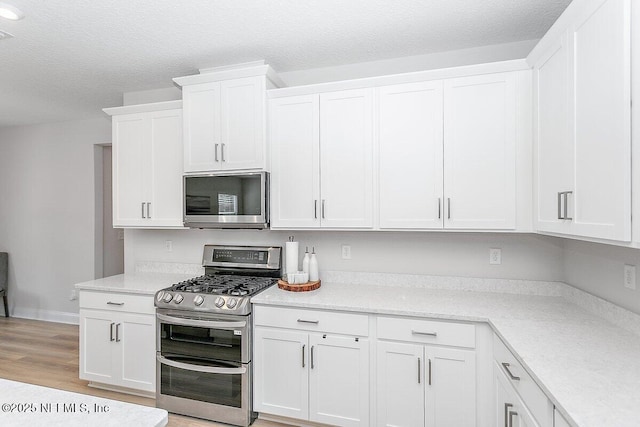 kitchen featuring stainless steel appliances, white cabinetry, a textured ceiling, and light wood-type flooring