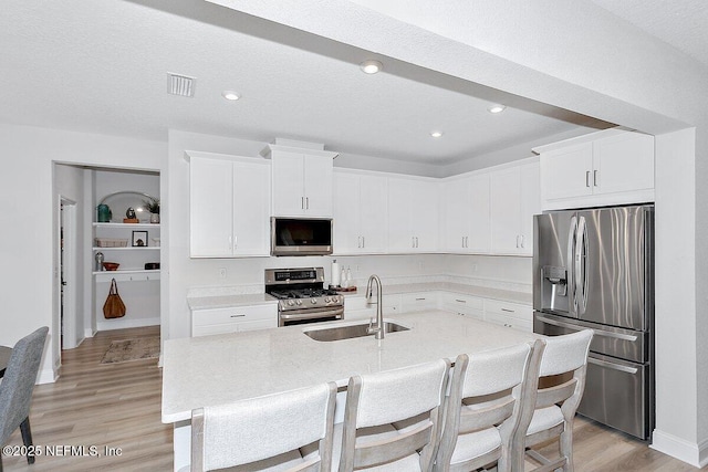 kitchen with white cabinetry, sink, stainless steel appliances, and a center island with sink