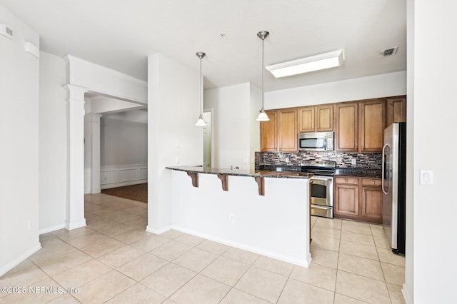 kitchen with decorative light fixtures, a kitchen bar, decorative backsplash, light tile patterned floors, and stainless steel appliances