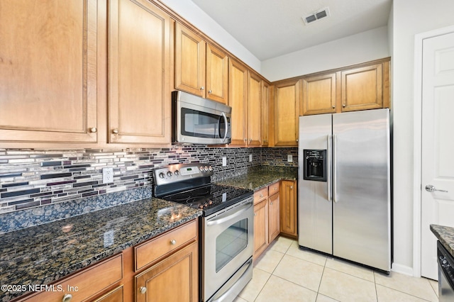 kitchen with backsplash, appliances with stainless steel finishes, dark stone counters, and light tile patterned floors