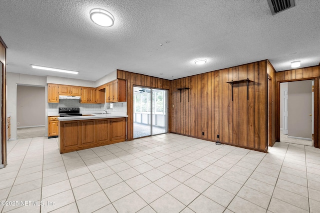 kitchen featuring black range with electric stovetop, light tile patterned floors, kitchen peninsula, and a textured ceiling