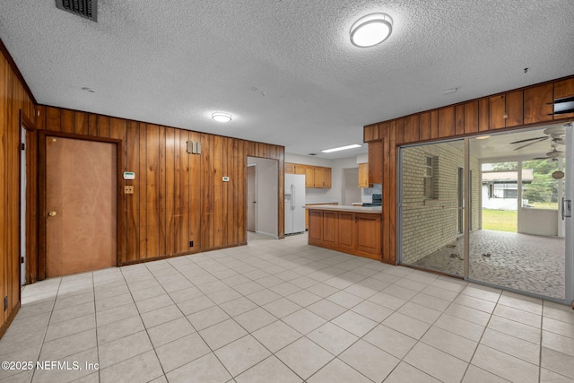 kitchen featuring white refrigerator with ice dispenser, light tile patterned floors, a textured ceiling, and wooden walls