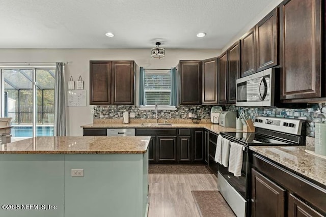 kitchen featuring a kitchen island, light stone countertops, appliances with stainless steel finishes, and sink