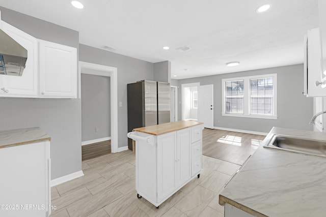 kitchen with sink, stainless steel refrigerator, white cabinetry, a center island, and ventilation hood