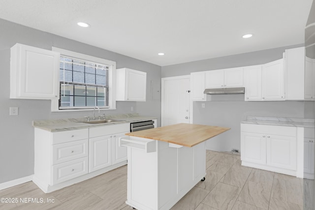 kitchen featuring sink, wooden counters, white cabinetry, a kitchen island, and stainless steel dishwasher