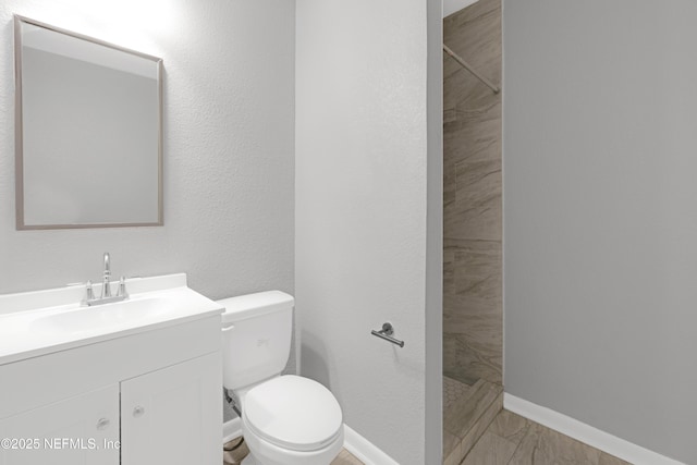 bathroom with vanity, a tile shower, and toilet