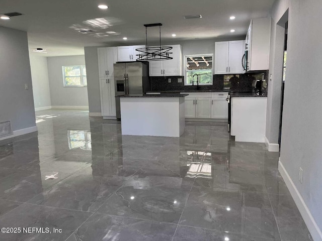 kitchen with pendant lighting, appliances with stainless steel finishes, backsplash, a center island, and white cabinets