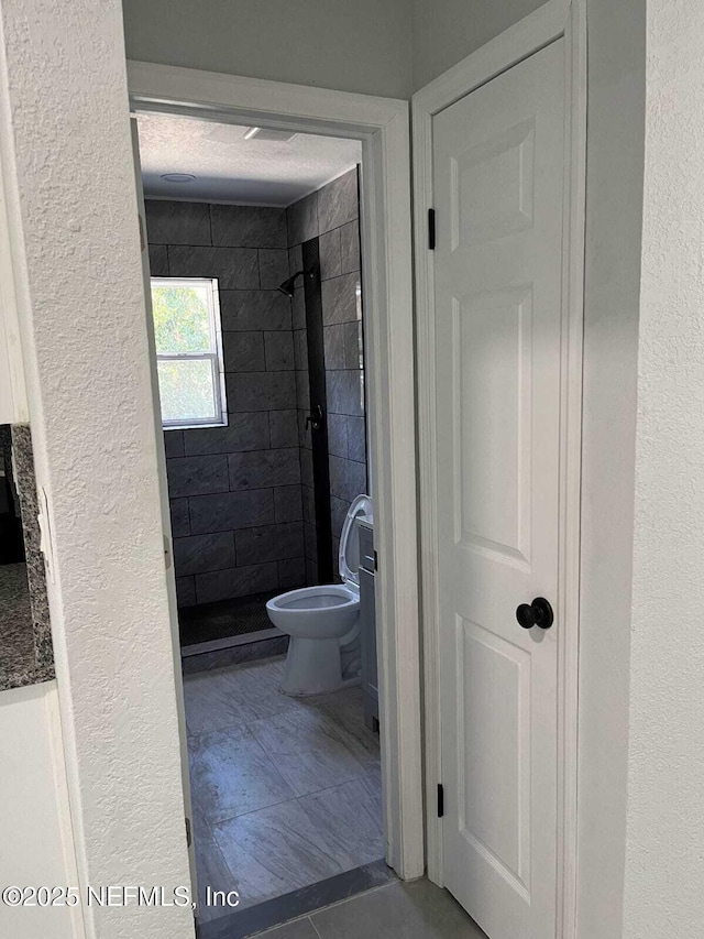 bathroom featuring a tile shower, tile patterned flooring, and toilet