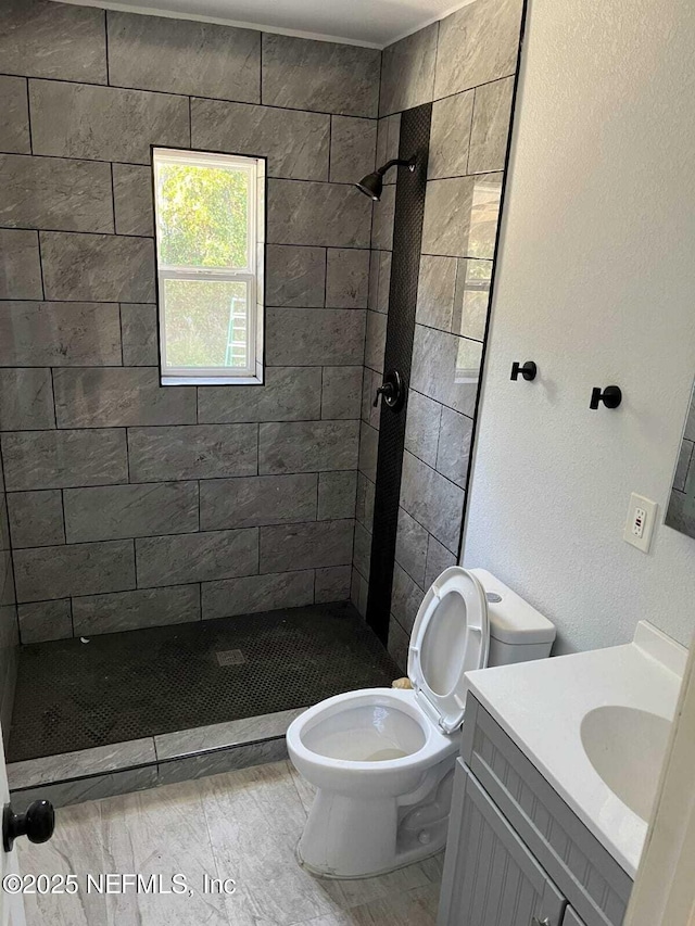 bathroom with tile patterned flooring, vanity, tiled shower, and toilet