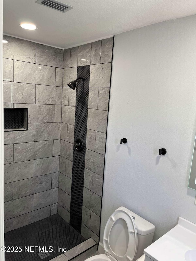 bathroom featuring a tile shower, vanity, and toilet