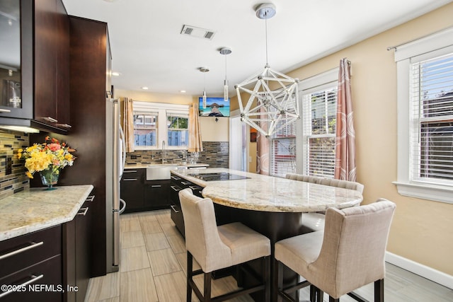 kitchen featuring a breakfast bar, tasteful backsplash, sink, light stone counters, and dark brown cabinets