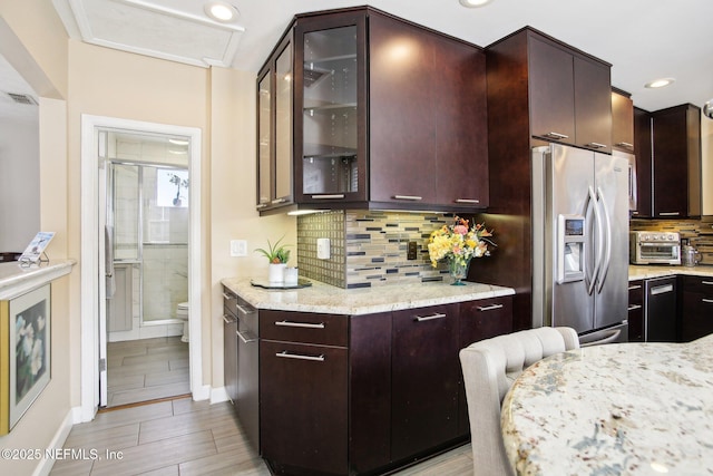 kitchen featuring light stone countertops, decorative backsplash, dark brown cabinetry, and stainless steel fridge with ice dispenser