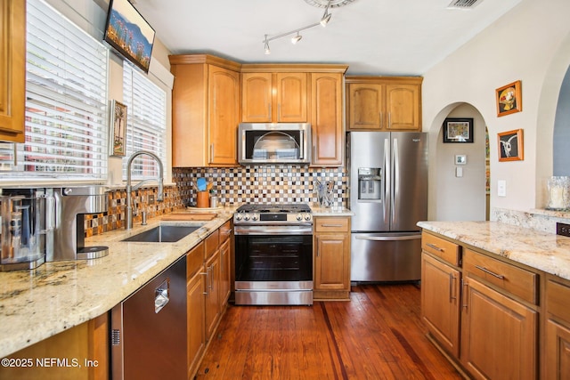 kitchen featuring appliances with stainless steel finishes, dark hardwood / wood-style floors, sink, decorative backsplash, and light stone countertops