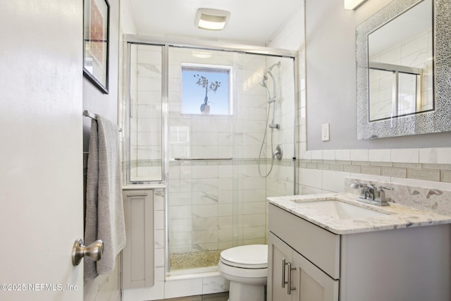 bathroom with tile walls, vanity, toilet, and walk in shower