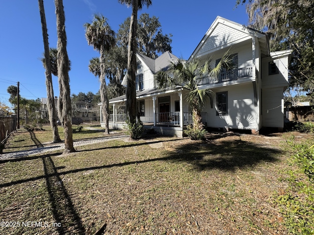 rear view of house with a yard, a balcony, and covered porch