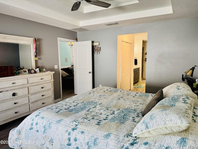 bedroom with dark wood-type flooring, a textured ceiling, ceiling fan, and ensuite bath