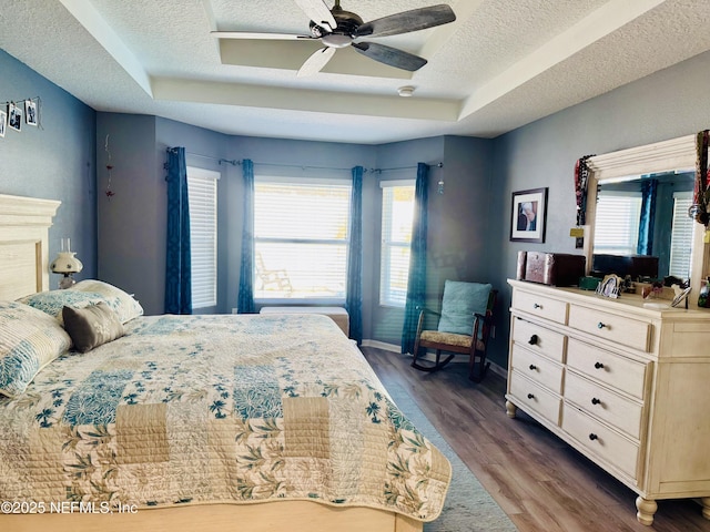 bedroom with a textured ceiling, wood-type flooring, a raised ceiling, and ceiling fan