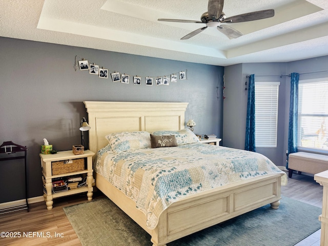 bedroom with a raised ceiling, wood-type flooring, a textured ceiling, and ceiling fan