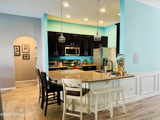 kitchen featuring sink, hanging light fixtures, stainless steel appliances, light stone countertops, and kitchen peninsula