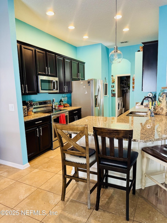 kitchen with sink, light tile patterned floors, appliances with stainless steel finishes, hanging light fixtures, and independent washer and dryer