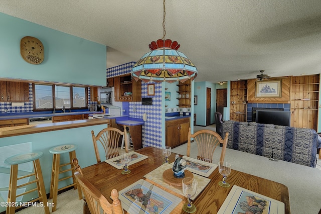 carpeted dining space with ceiling fan, a fireplace, sink, and a textured ceiling