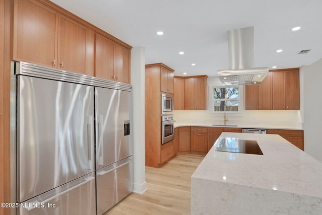 kitchen featuring island range hood, sink, built in appliances, light stone counters, and light hardwood / wood-style flooring