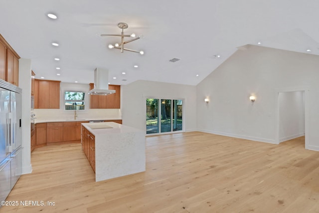 kitchen with light hardwood / wood-style flooring, high vaulted ceiling, a notable chandelier, island exhaust hood, and stainless steel built in fridge