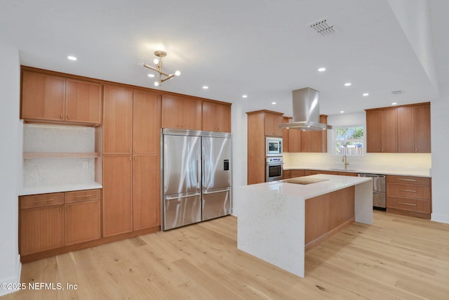 kitchen with island range hood, a center island, built in appliances, and light hardwood / wood-style flooring