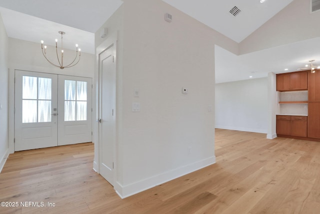 entryway featuring lofted ceiling, an inviting chandelier, light wood-type flooring, and french doors