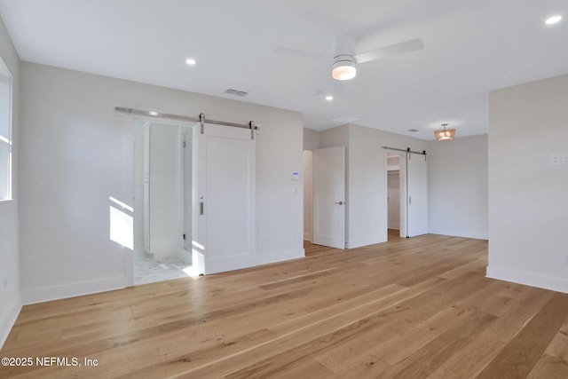 unfurnished room featuring ceiling fan, a barn door, and light hardwood / wood-style flooring