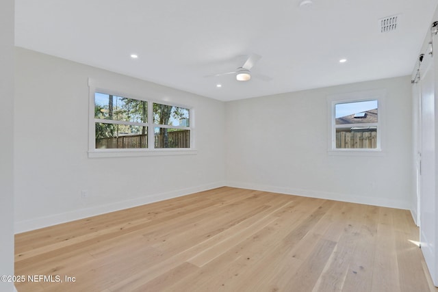 spare room featuring ceiling fan, a barn door, a healthy amount of sunlight, and light hardwood / wood-style floors