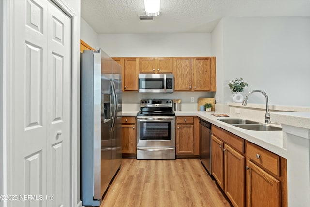 kitchen featuring sink, light stone counters, stainless steel appliances, a textured ceiling, and light hardwood / wood-style flooring