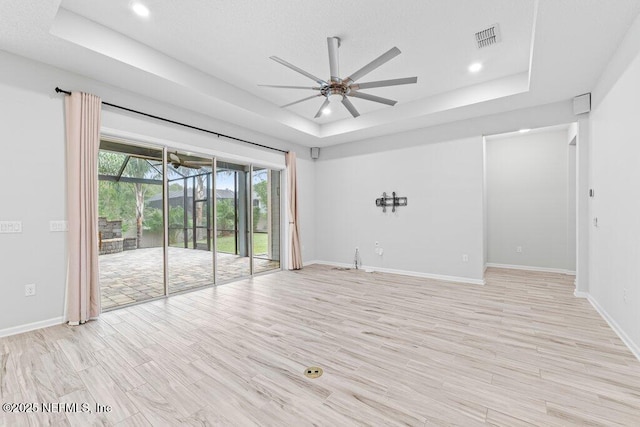 unfurnished room featuring a tray ceiling, light hardwood / wood-style floors, and ceiling fan