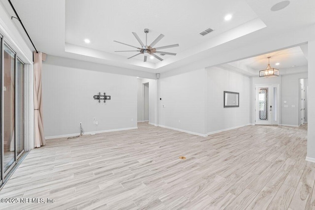 unfurnished living room with a raised ceiling, ceiling fan with notable chandelier, and light wood-type flooring