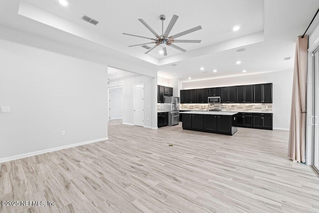 kitchen featuring a tray ceiling, light wood-type flooring, an island with sink, and appliances with stainless steel finishes