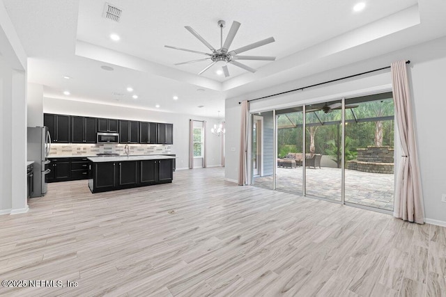 kitchen with a center island with sink, light hardwood / wood-style floors, a raised ceiling, and appliances with stainless steel finishes