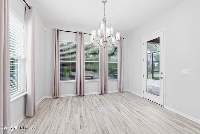 unfurnished dining area with an inviting chandelier, a wealth of natural light, and light hardwood / wood-style floors