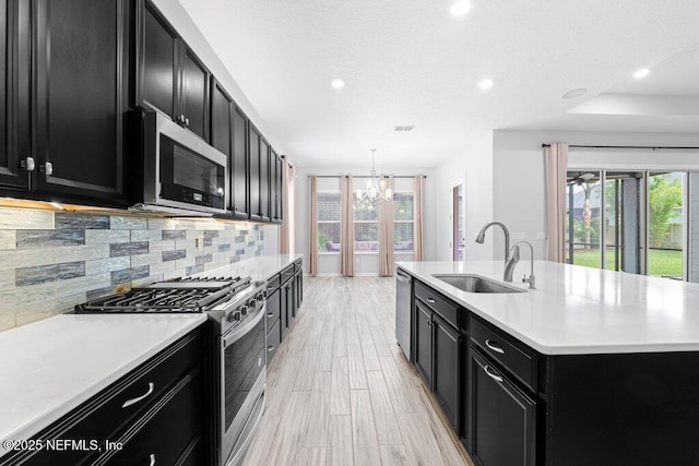 kitchen featuring appliances with stainless steel finishes, tasteful backsplash, sink, a kitchen island with sink, and light wood-type flooring