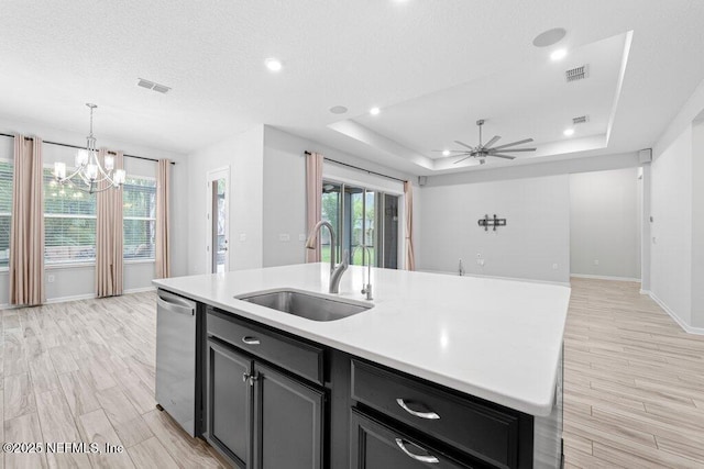 kitchen featuring sink, decorative light fixtures, a raised ceiling, dishwasher, and a kitchen island with sink