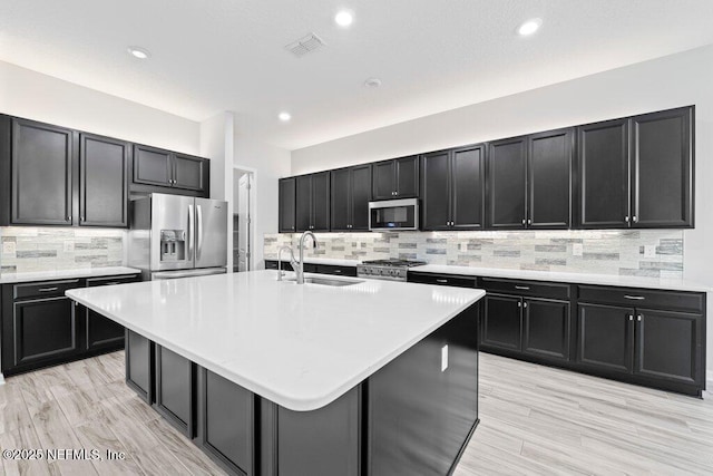 kitchen featuring an island with sink, appliances with stainless steel finishes, sink, and light hardwood / wood-style flooring