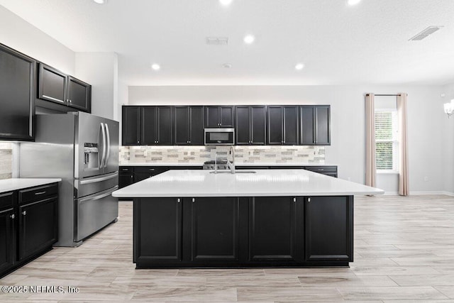 kitchen with a kitchen island with sink, sink, backsplash, and stainless steel appliances